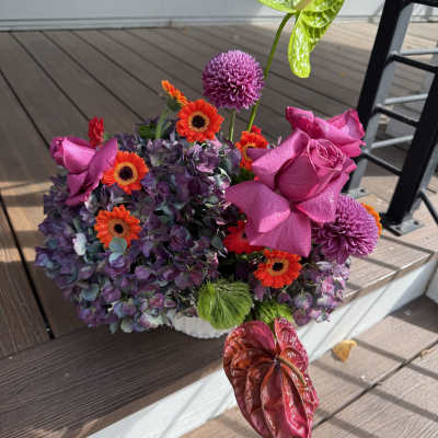 Bright mixed floral arrangement with pink roses and purple blooms in a white container