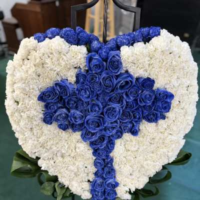 Heart-shaped floral tribute with blue roses and white carnations on an easel
