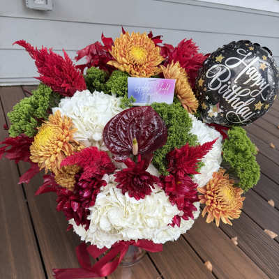 Mixed red, white, and orange floral arrangement with a birthday balloon