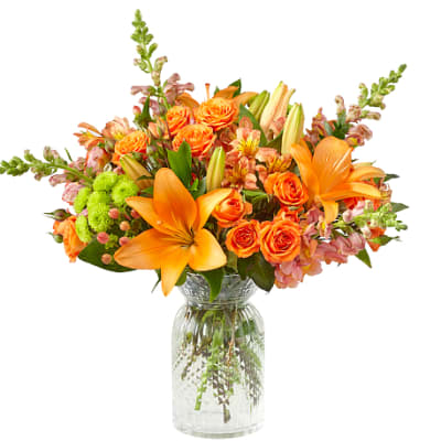 Orange lilies and roses arranged in a clear glass vase