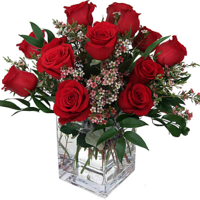 Red roses arranged in a clear square glass vase with small pink filler flowers