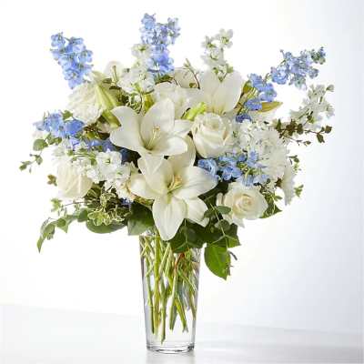 White lilies and roses with blue flowers in a clear glass vase
