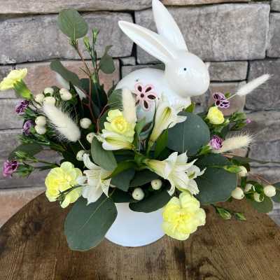 White bunny figurine surrounded by yellow and white flowers in a vase