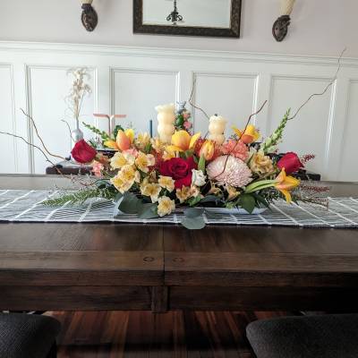 Low floral centerpiece with roses, lilies, and chrysanthemums in warm pink and yellow tones