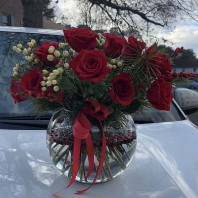 Red roses in a round glass vase with berries and a red ribbon