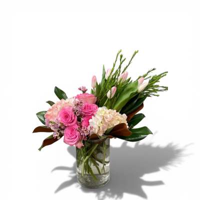 Arrangement of pink roses, pale tulips, and blush hydrangeas in a clear glass vase