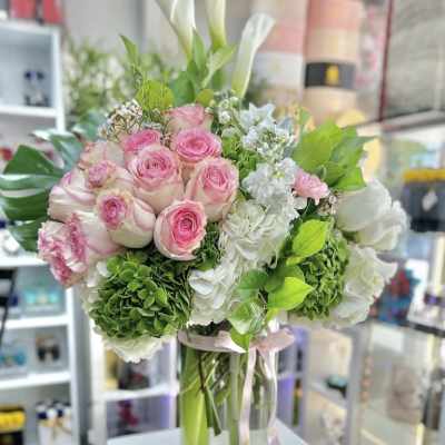 Tall arrangement of pink roses, white calla lilies, and green and white hydrangeas in a clear glass vase.