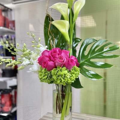 Tall arrangement of white calla lilies, pink roses, green hydrangea and orchids in a clear glass vase