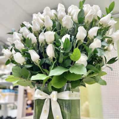 Arrangement of white rosebuds in a clear square vase with white ribbon