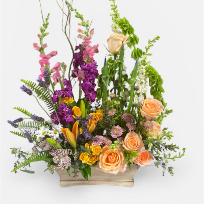 Colorful mixed arrangement of peach roses, yellow lilies, and purple flowers in a wooden box.