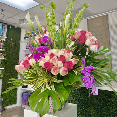 Large arrangement of pink and white roses with purple orchids and calla lilies in a glass vase