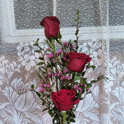Three red roses in a glass vase with a small white teddy bear