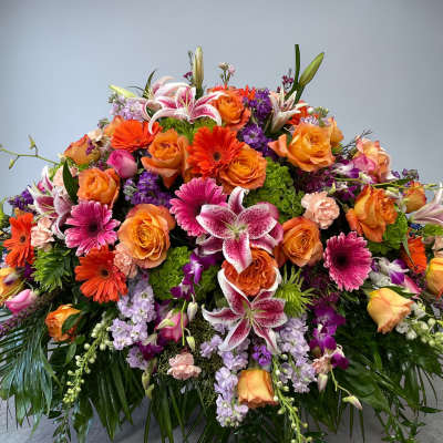Large low arrangement of orange roses, pink lilies, gerbera daisies and purple flowers in a dome shape