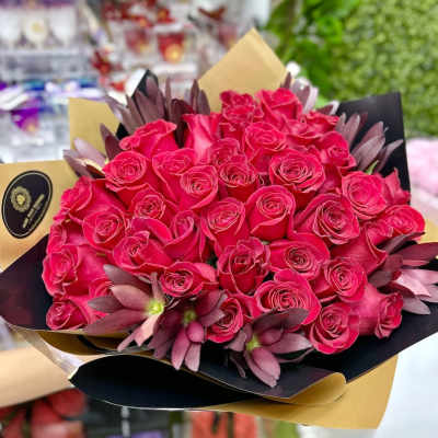 Large bouquet of hot pink roses with purple blooms wrapped in black and gold paper.