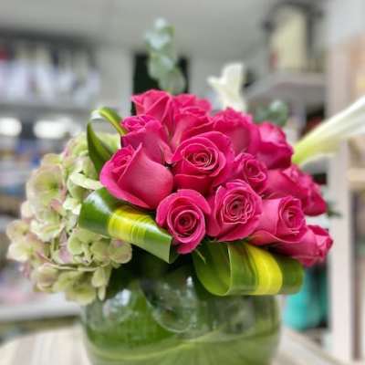 Low glass vase of hot pink roses with pale green hydrangeas and looped green leaves.