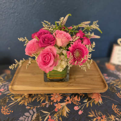 Pink roses and a gerbera daisy arranged in a square glass vase