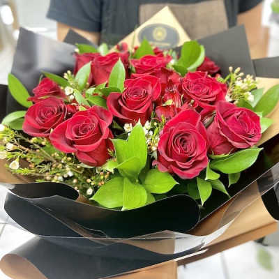 Hand-tied bouquet of red roses with small white filler flowers in black and tan wrap