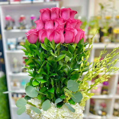 Tall arrangement of pink roses, layered greenery, and white hydrangeas in a pink hatbox.