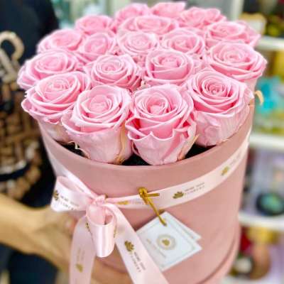 Pink hat box filled with tightly packed light pink roses and tied with a matching ribbon