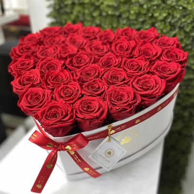 Heart-shaped white box filled with tightly packed red roses and a red ribbon bow.