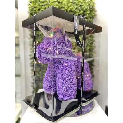 Purple rose-covered teddy bear in a clear display box with a black base and lid.