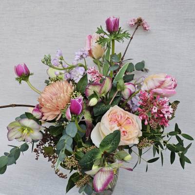 Loose arrangement of pink and peach blooms, including roses and tulips, in a clear glass vase