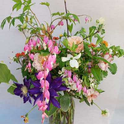 Loose garden-style bouquet of pink, purple, and peach flowers in a clear glass vase
