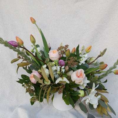Wide peach rose and tulip arrangement with white orchids and stock in a white vase