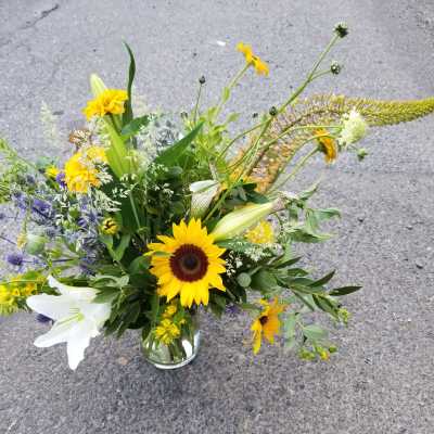 Loose mixed bouquet with sunflowers, white lilies and yellow daisies in a clear glass vase