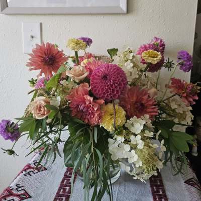 Loose garden-style arrangement of pink dahlias, roses, and white hydrangeas in a clear glass vase