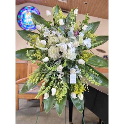 Tall white and green standing floral spray on an easel in a church setting