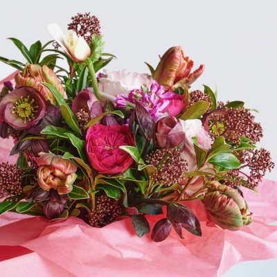 Hand-tied bouquet of pink and burgundy blooms wrapped in pink tissue paper.