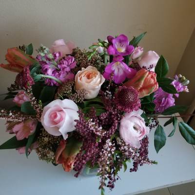 Low pink and purple flower arrangement with roses and tulips in a clear glass vase