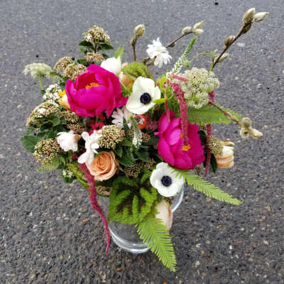 Mixed arrangement of hot pink blooms, white anemones, and peach roses in a clear glass vase