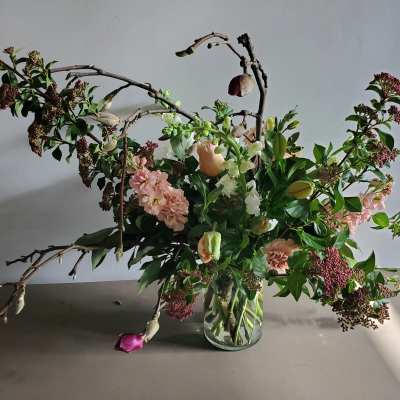 Asymmetrical arrangement of pink and peach flowers with branches in a clear glass vase