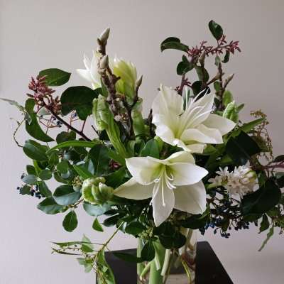 Tall arrangement of white amaryllis and other white blooms in a clear glass vase