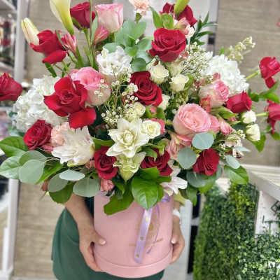 Tall arrangement of red and pink roses with white blooms and calla lilies in a pink hatbox container