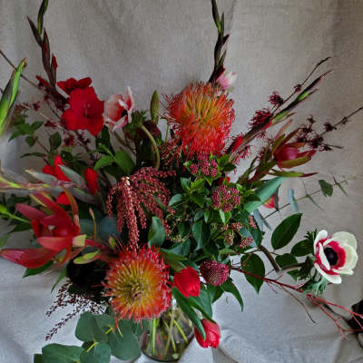 Tall red and white floral arrangement with pincushion protea in a clear glass vase.