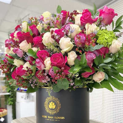Large arrangement of hot pink and cream roses with accents in a black hat box container