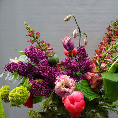 Tall mixed arrangement with purple lilacs, pink fringe tulips, and red blooms in a glass vase.