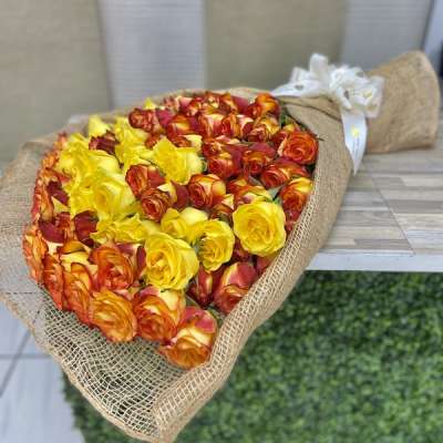 Large bouquet of yellow and orange-red roses wrapped in burlap with a white bow.