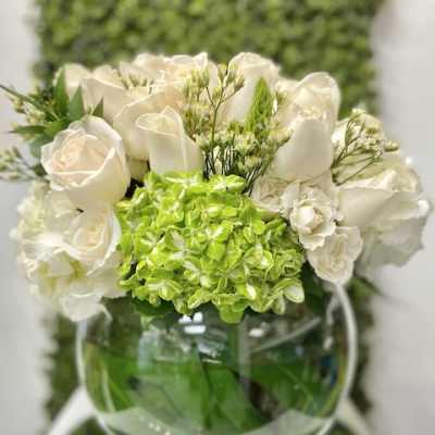 Low arrangement of white roses and green hydrangea in a round glass bowl vase