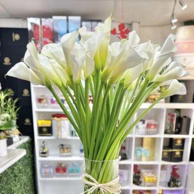 Tall bundle of white calla lilies in a clear glass vase tied with raffia