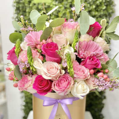 Pink and white roses with pink gerbera daisies arranged in a gold hatbox with a lavender ribbon