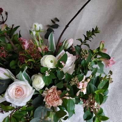 Loose arrangement of blush roses, white ranunculus, and pink flowers with branching accents