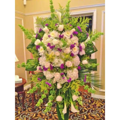 Tall standing spray of white and purple flowers with abundant green accents on an easel.