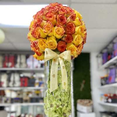 Tall glass vase with yellow and orange rose sphere and green orchids inside the vase