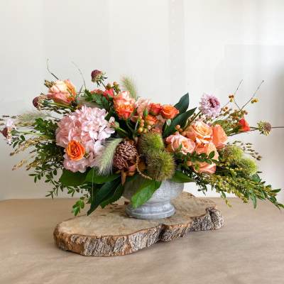 Low floral arrangement in a metal urn with peach and pink blooms