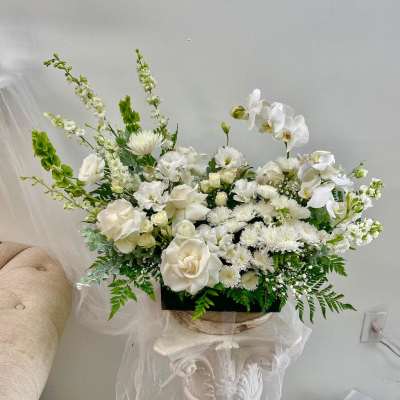 White floral arrangement with orchids and roses in a low container
