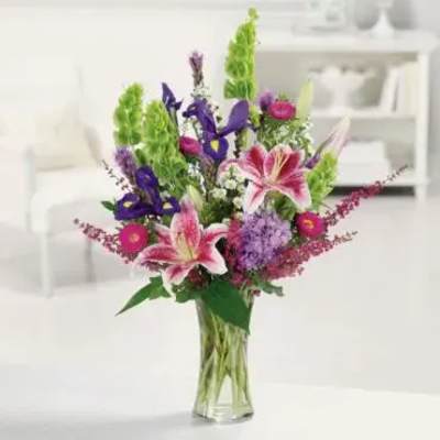 Bouquet of pink lilies, purple irises, and green snapdragons in a glass vase